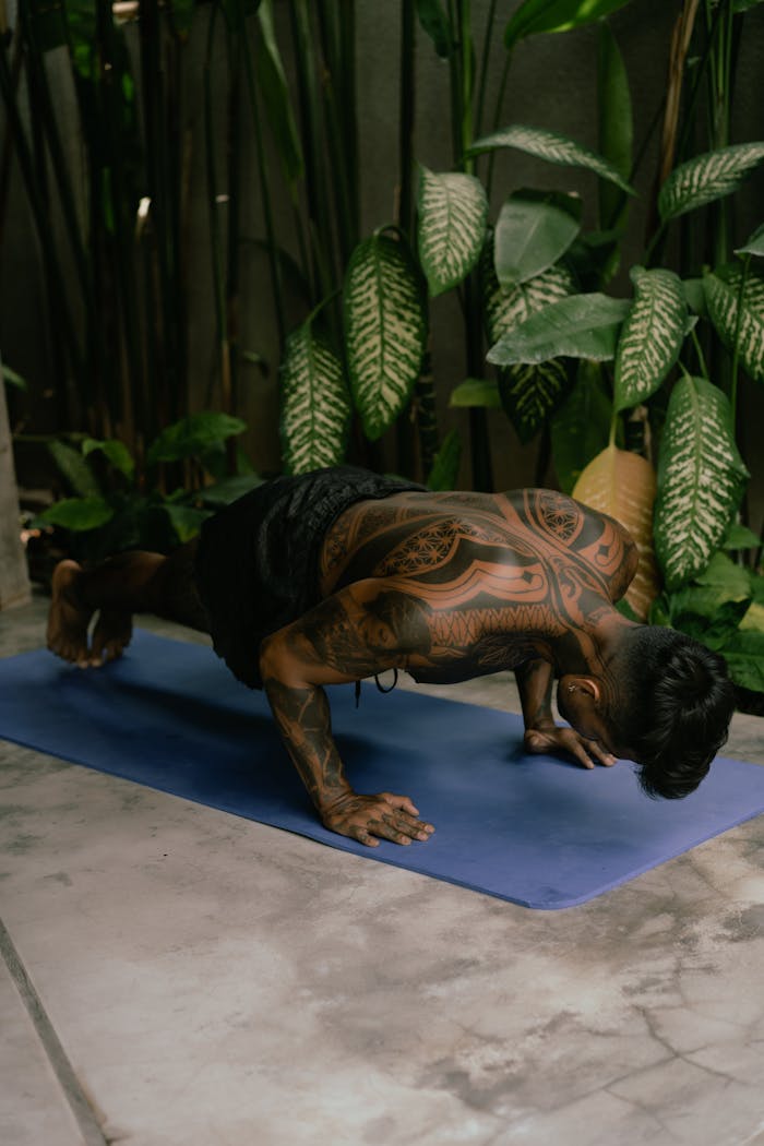 Tattooed young man performs push-ups indoors on a mat, emphasizing fitness and strength.